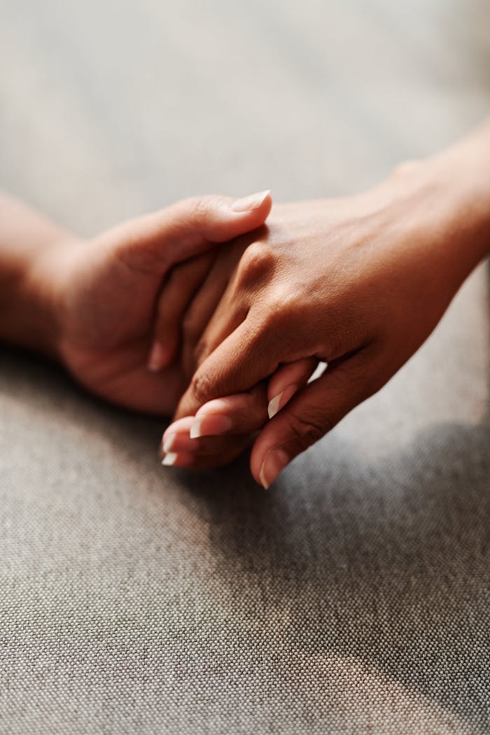 A close-up of two hands clasped together on a grey textile background, symbolizing unity.